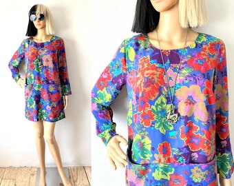 Puede incluir: Un vestido de estampado floral azul con mangas largas y un collar con un colgante plateado. El vestido tiene un corpiño ajustado y una falda suelta y fluida.