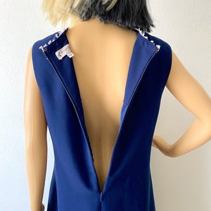 May include: A navy blue sleeveless dress with a white beaded neckline and a back zipper. The dress is on a mannequin.