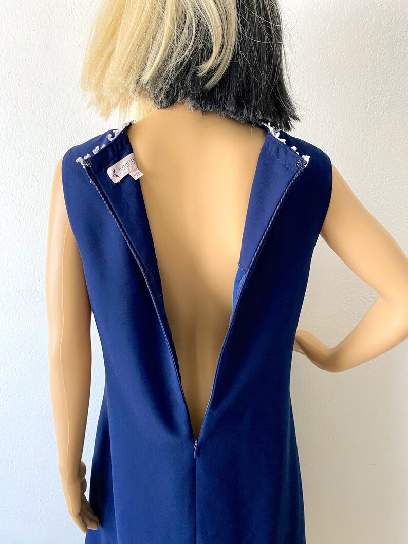 May include: A navy blue sleeveless dress with a white beaded neckline and a back zipper. The dress is on a mannequin.
