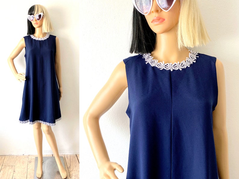 May include: A sleeveless navy blue dress with a white lace trim around the neckline. The dress has a slightly flared skirt and a simple, elegant design.