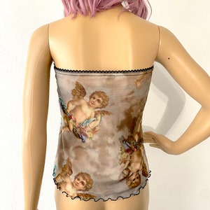Puede incluir: Un top de malla marr&oacute;n transparente con ribete negro y estampado de querubines con alas y flores. El top es de tirantes.