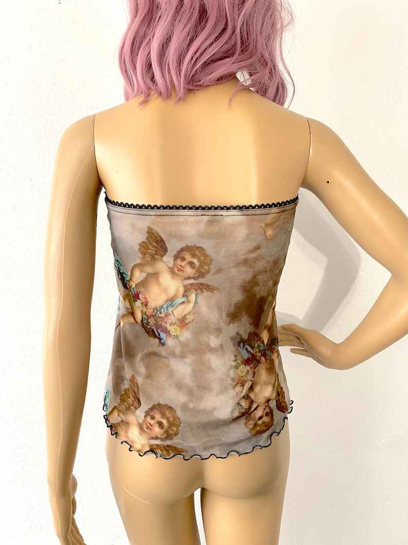 Puede incluir: Un top de malla marr&oacute;n transparente con ribete negro y estampado de querubines con alas y flores. El top es de tirantes.