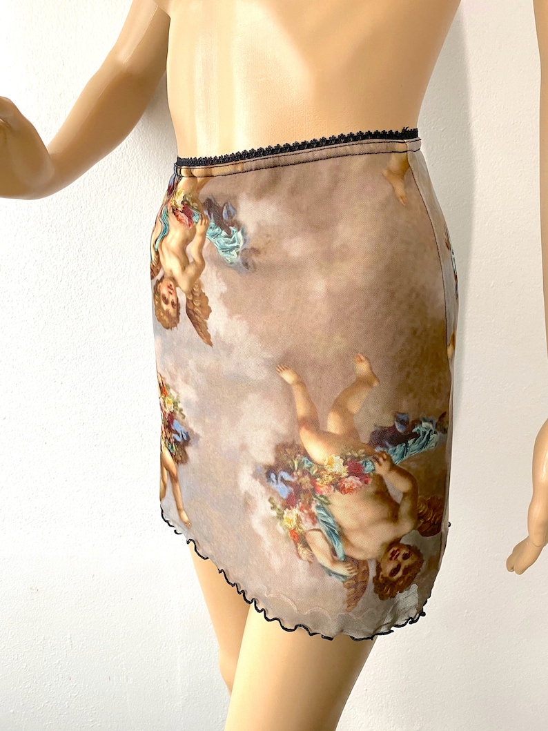 Puede incluir: Una falda corta y transparente con un estampado de querubines marrones y blancos. La falda tiene una cintura el&aacute;stica negra y un dobladillo festoneado.