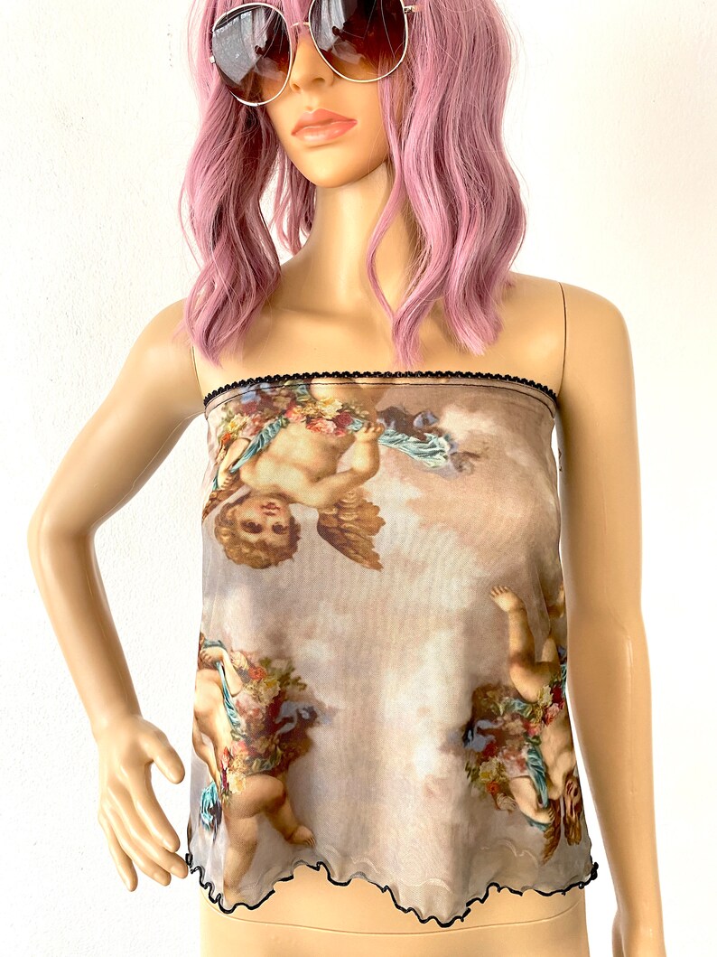 Puede incluir: Un top de malla marr&oacute;n transparente con ribete negro. El top presenta un estampado de querubines con alas y flores sobre un fondo nublado.