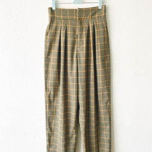 May include: High-waisted, wide-leg pants in a brown and yellow plaid pattern. The pants have pleats in the front and a button closure.