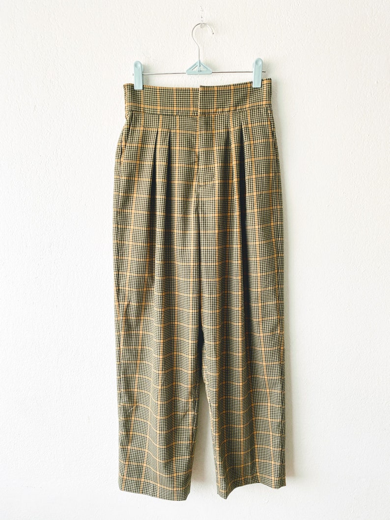 May include: High-waisted, wide-leg pants in a brown and yellow plaid pattern. The pants have pleats in the front and a button closure.