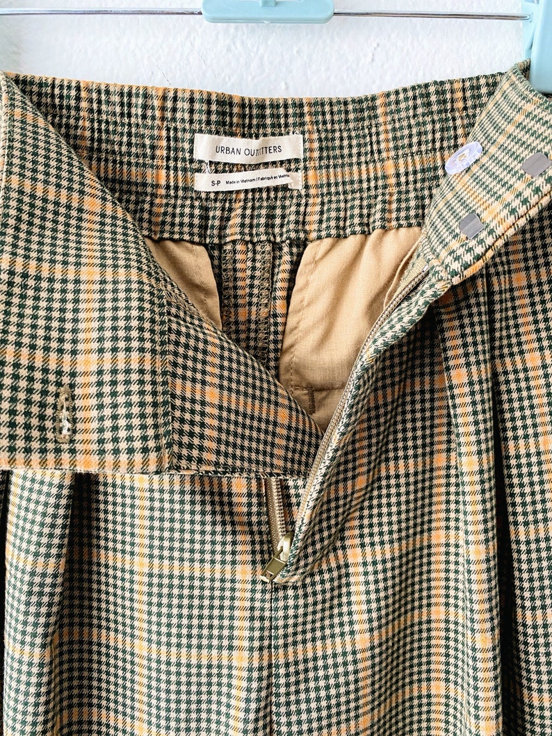 May include: Green and yellow plaid pants with a zipper closure and a label that reads "Urban Outfitters".