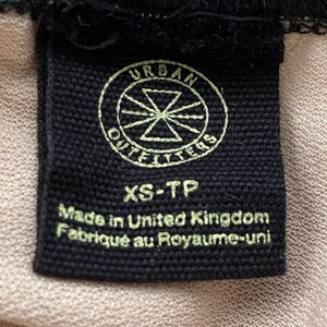Puede incluir: Etiqueta de ropa negra con texto blanco que dice "Urban Outfitters" en un c&iacute;rculo con una estrella en el centro. Debajo del c&iacute;rculo, el texto dice "XS-TP" y "Made in United Kingdom Fabriqu&eacute; au Royaume-Uni."