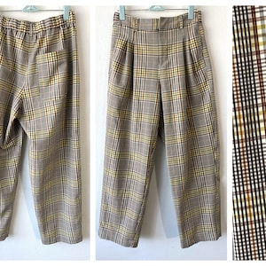May include: Brown plaid pants with yellow and black accents. The pants have a high waist, pleats, and a straight leg. The fabric has a classic plaid pattern. The pants are hanging on a white background.