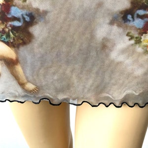 Puede incluir: Una falda de malla transparente con ribete negro y un estampado vintage de un querub&iacute;n y flores.