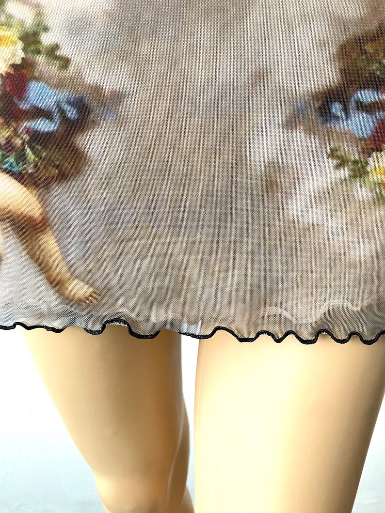 Puede incluir: Una falda de malla transparente con ribete negro y un estampado vintage de un querub&iacute;n y flores.