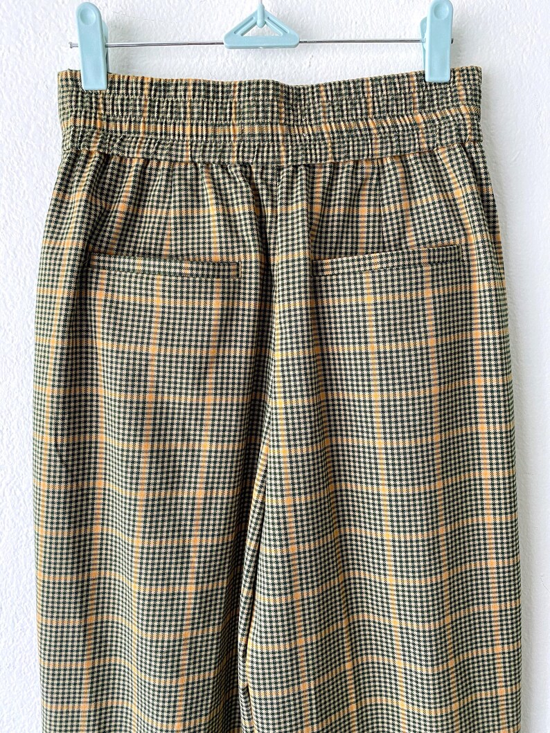 May include: A pair of brown and yellow plaid pants with an elastic waistband. The pants have two back pockets.
