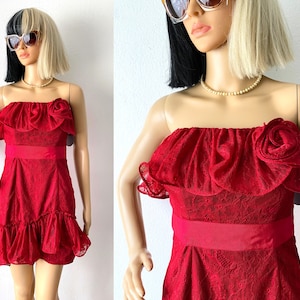 May include: A red strapless dress with a lace bodice and a ruffled skirt. The dress has a large rose embellishment on the bodice.