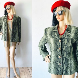 May include: A green snakeskin patterned blazer with a button closure. The blazer has a collar and long sleeves. The model is wearing a red beret and sunglasses.