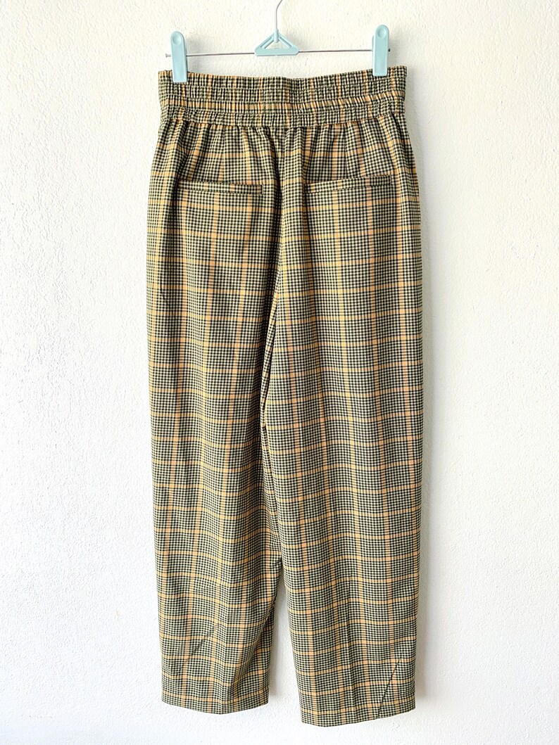 May include: A pair of brown and yellow plaid pants with an elastic waistband. The pants have a relaxed fit and are cropped at the ankle.