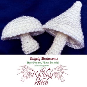May include: Two white crochet mushrooms with textured caps and stems are displayed against a dark blue background. The image includes text that reads "Fidgety Mushrooms - Base Pattern, Photo Tutorial - A crochet pattern by the Restless Witch."