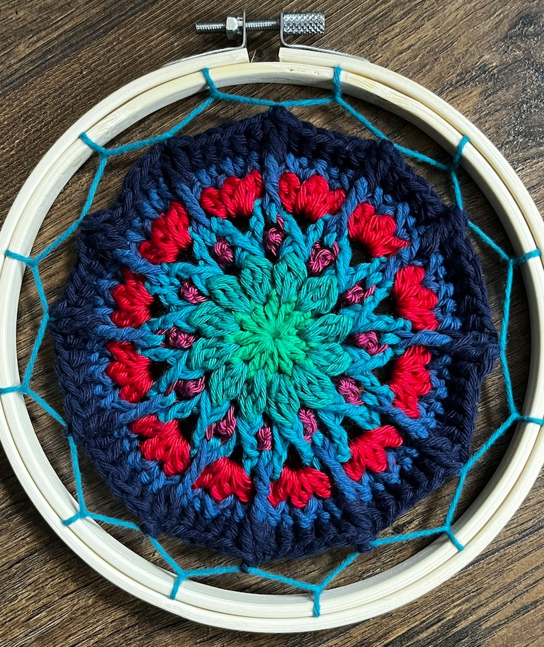 May include: A crocheted mandala with a blue, green, and red color gradient, framed in a wooden hoop with a turquoise string.