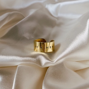 May include: A gold-toned ring with the words "HE HIM" engraved on the band.