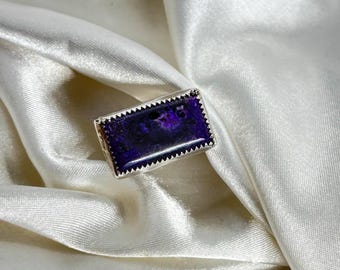 May include: A silver ring with a rectangular purple gemstone set in a silver bezel.