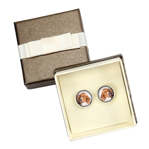 May include: A pair of earrings in a gift box. The earrings are round and feature a photo of a brown and white dog.