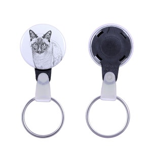 Può includere: Un portachiavi rotondo con un cordino retrattile e un anello di metallo. Un gatto bianco e grigio con gli occhi blu è raffigurato sul portachiavi.