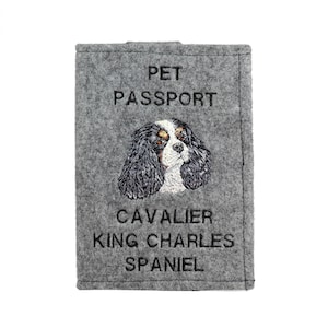 May include: Gray felt pet passport holder with an embroidered Cavalier King Charles Spaniel and the text "PET PASSPORT".