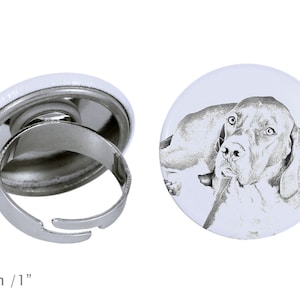 Könnte beinhalten: Ein verstellbarer Silberring mit einem weißen Knopf, der eine Schwarzweißillustration eines Hundekopfes zeigt. Der Knopf hat einen Durchmesser von 2,5 cm.