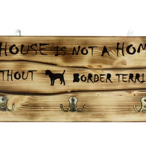 Border Terrier, a wooden wall peg, hanger with the picture of a dog and the words: &quot;A house is not a home without...&quot;