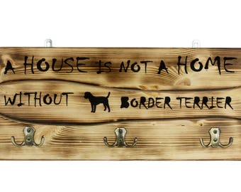 Border Terrier, a wooden wall peg, hanger with the picture of a dog and the words: "A house is not a home without..."