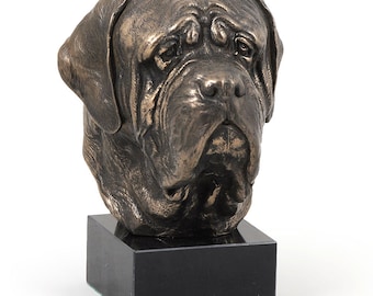 May include: A bronze-colored sculpture of a Mastiff dog head with detailed facial wrinkles and floppy ears. The sculpture is mounted on a solid, rectangular black base, providing a stable foundation for the detailed canine bust display.