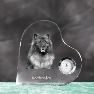 Könnte beinhalten: Eine herzförmige Uhr aus klarem Glas mit einem Schwarz-Weiß-Bild eines Keeshond-Hundes. Die Uhr hat ein kleines, rundes analoges Zifferblatt mit silbernen Zeigern und einer silbernen Lünette. Das Wort "Keeshonden" ist aufgedruckt.
