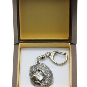 May include: A silver-colored keychain featuring a detailed head of a Chow Chow dog. The keychain is in a brown gift box with a white interior.