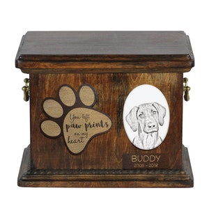 May include: A wooden pet urn with a paw print design and the text "You left paw prints on my heart". The urn has a portrait of a dog and a nameplate that reads "Buddy 2005-2018".