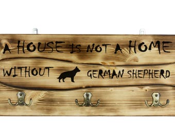 German Shepherd, a wooden wall peg, hanger with the picture of a dog and the words: "A house is not a home without..."