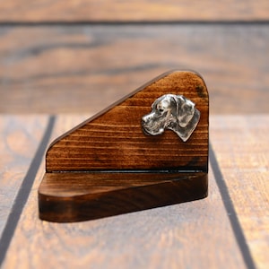 Puede incluir: Un estante de madera con una escultura de cabeza de perro plateada en la parte delantera. El estante está teñido de un color marrón oscuro y tiene un borde biselado.