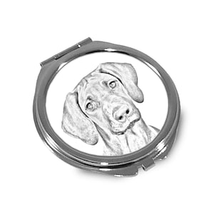 Può includere: Uno specchio compatto argentato con un'illustrazione in bianco e nero di una testa di cane. Il cane ha le orecchie cadenti e guarda di lato.