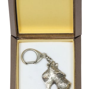 Puede incluir: Un llavero de cabeza de perro terrier escocés de color plateado en una caja de regalo marrón con interior blanco.