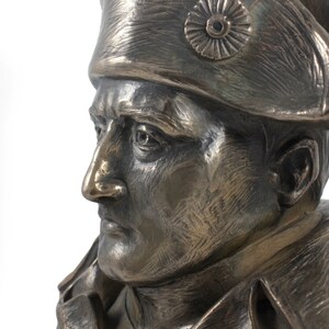 Op de afbeelding: Bronzen bustebeeld van een man met een militaire hoed met een decoratief embleem. De buste is gedetailleerd met realistische kenmerken en een gestructureerd oppervlak.