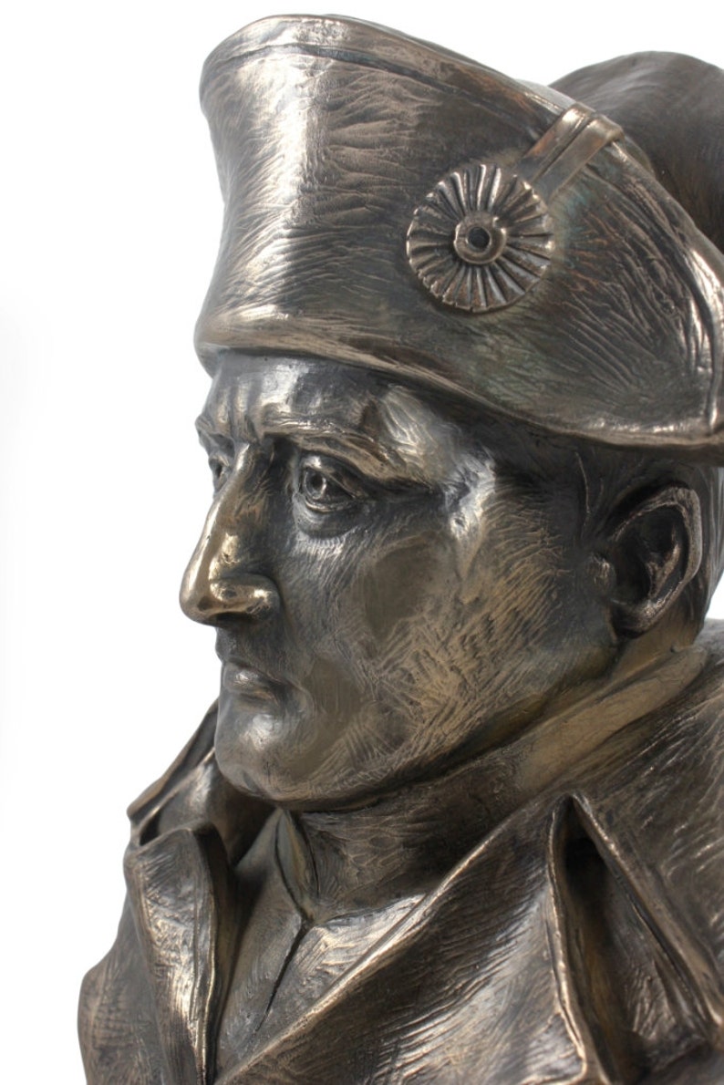 Op de afbeelding: Bronzen bustebeeld van een man met een militaire hoed met een decoratief embleem. De buste is gedetailleerd met realistische kenmerken en een gestructureerd oppervlak.