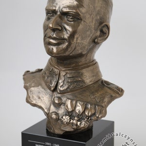 May include: Bronze bust sculpture of a man in military uniform with medals on his chest. The bust is on a black base with a plaque that reads "1901-1948 WITOLD PILECKI" and a quote in Polish.