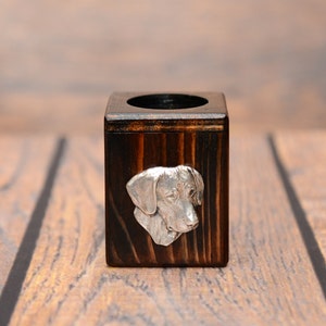 May include: A small wooden pencil holder with a silver dog head design on the front. The holder is dark brown and has a square shape.