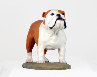 Könnte beinhalten: Eine weiße und braune Bulldoggen-Figur mit schwarzer Nase und schwarzen Augen. Die Figur steht auf einem braunen Sockel.