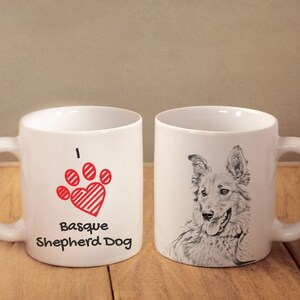 Peut inclure: Deux mugs en céramique blancs. L'un présente un motif de cœur en forme de patte rouge avec le texte "I Basque Shepherd Dog". L'autre mug a une illustration en noir et blanc d'un visage de chien.