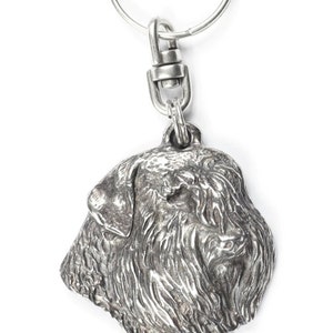 Könnte beinhalten: Ein silberfarbener Metall-Schlüsselanhänger mit einer detaillierten Reliefskulptur eines Hundekopfes mit zotteligem Fell. Der Anhänger misst 4,7 cm mal 4,3 cm in der Höhe und 4,2 cm in der Breite bei einem Gesamtgewicht von 33 Gramm.