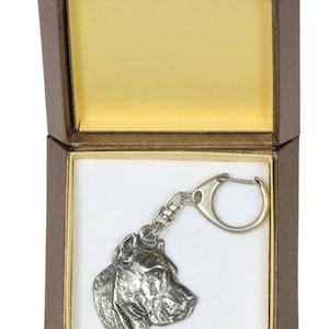 May include: A silver-colored dog head keychain in a brown gift box with a yellow interior. The keychain is of a Cane Corso breed dog.