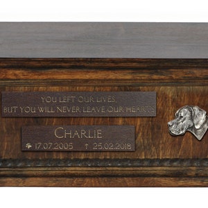 May include: A wooden pet urn with a brown finish. The urn has a plaque with the inscription "YOU LEFT OUR LIVES, BUT YOU WILL NEVER LEAVE OUR HEARTS."  A second plaque reads "CHARLIE 17.07.2005 † 25.02.2018". A metal dog head is attached to the urn.