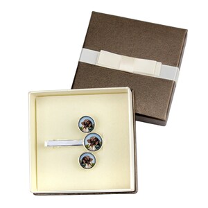 May include: A gift box containing a silver tie bar and three cufflinks with a brown and white dog image. The box is brown with a white ribbon and bow.