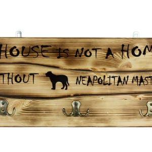 Op de afbeelding: Een houten bord met drie haken met de tekst "Een huis is geen thuis zonder een Napolitaanse Mastiff". Het bord heeft een gebrande houtlook en een silhouet van een Napolitaanse Mastiff.