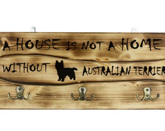 Australian terrier, a wooden wall peg, hanger with the picture of a dog and the words: "A house is not a home without..."