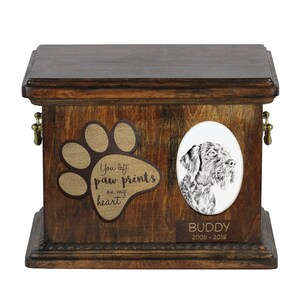 May include: A wooden pet urn with a paw print design and the text "You left paw prints on my heart". The urn has a portrait of a dog and a nameplate that reads "BUDDY 2005-2018".
